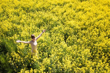 Sarı çiçek açan kolza tohumu tarlasında duran genç bir kadının hava manzarası..