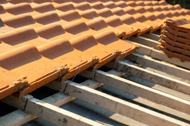 Üst üste binen sarı seramik çatı kiremitleri ahşap tahtalara monte edilmiş inşaat halindeki binanın çatısını kaplıyor..