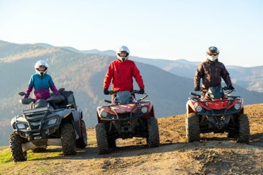Koruyucu kasklı mutlu sürücüler günbatımında ATV dörtlü motosiklet sürüşünün keyfini çıkarıyorlar..
