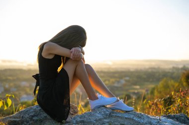 Siyah kısa yaz elbisesi içinde depresif genç bir kadın bir dağ tepesinde oturuyor ve gün batımında açık havayı düşünüyor. Yalnız bir kadın, doğada sıcak bir akşamda tefekkür ediyor..