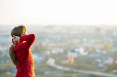 Kırmızı ceketli genç bir kadın ellerini başının arkasına koyup akşam manzarasının keyfini çıkarıyor. Rahatlama, özgürlük ve sağIık kavramı.