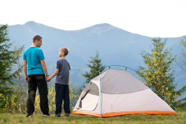 Küçük oğluyla birlikte yaz dağlarında yürüyüş çadırının yanında duran genç bir baba. Aktif aile eğlencesi kavramı.