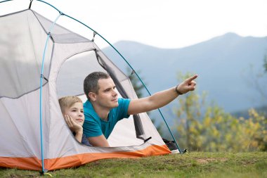 Oğlu ile birlikte yaz dağlarında kamp çadırında dinlenen genç bir baba. Aktif aile eğlencesi kavramı.