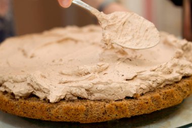 Evde kek pişirme süreci. Çikolatalı bisküvinin üzerine kadın el kreması dök. Mutfak ve lezzetli tatlı konsepti.