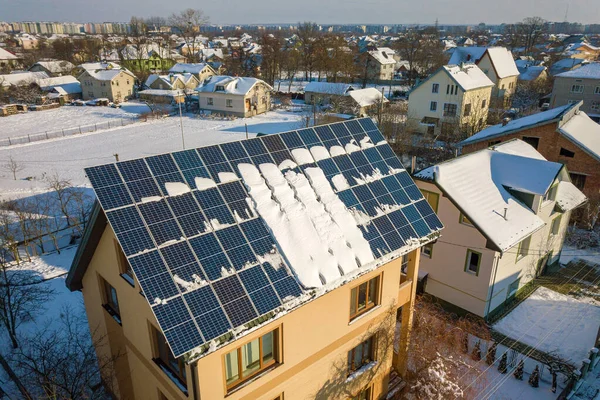 House roof covered with solar panels in winter with snow on top. Energy efficiency and maintenance concept.