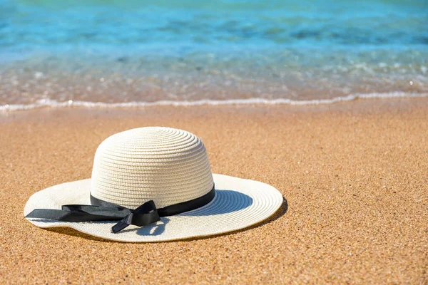 White woman straw hat laying on tropical sand beach with blue vibrant ocean water in background on sunny summer day. Vacations and destination travel concept.