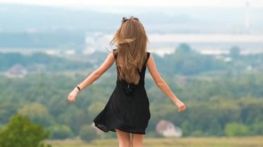 Kısa yaz elbisesi içinde, açık havada mutlu bir şekilde dans eden genç bir kadının arka görüntüsü..