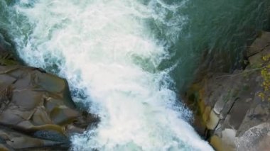 Nehir şelalesinin havadan görünüşü berrak turkuaz suyu kalın beyaz köpüklü ıslak kayaların arasına düşüyor..