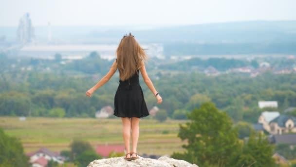 穿着黑色短裙站在山顶上享受夏日温暖的年轻而快乐的女人 — 图库视频影像