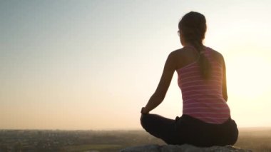 Genç, rahat bir kadın büyük bir taşın üzerinde oturmuş sıcak bir yaz gününün tadını çıkarıyor. Gün batımında meditasyon yapan ve dinlenen bir kız..