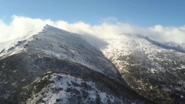 Yeşil ladin ormanları ve yüksek karlı tepelerle kaplı görkemli dağların havadan görünüşü.