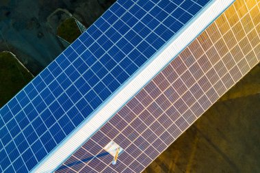 Temiz ekolojik elektrik üretmek için çatıya monte edilen mavi fotovoltaik güneş panellerinin havadan görünüşü. Yenilenebilir enerji konsepti üretimi.