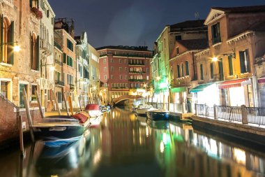 İtalya, Venedik 'teki kanallarda aydınlatılmış eski mimari, yüzen tekneler ve ışık yansımaları gece görüşü.