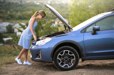 Kaputu açık, bozuk bir arabanın yanında duran genç bir kadın sürücü aracıyla sorun yaşıyor..