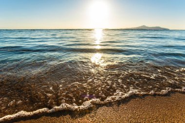 Yazın güneşli sahillerde, sarı kumsal üzerinde açık mavi suyla küçük deniz dalgalarını kapatın..