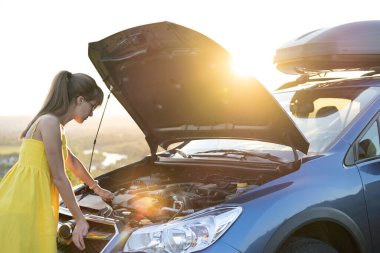 Genç bir kadın sürücü kaputu açık bir şekilde arabasının yanında duruyor..