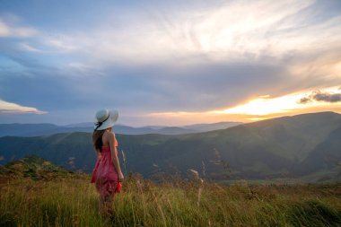 Kırmızılı genç kadın sonbahar dağlarında rüzgarlı bir akşamda çimlerde yürüyor..