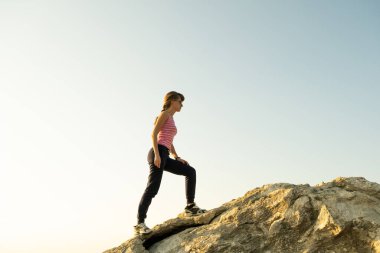 Güneşli bir günde kadın yürüyüşçü dik kayalara tırmanıyor. Genç bayan dağcı zor tırmanma rotasının üstesinden gelir. Doğada aktif eğlence kavramı.