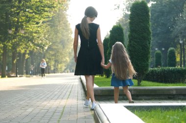 Annemin ve uzun saçlı küçük kızının yaz parkında el ele tutuşup yürürken görüntüsü..