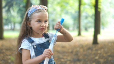 Yeşil Park 'ın dışında sabun köpüğü üfleyen mutlu küçük kız çocuğu. Çocuklar için açık hava yaz aktiviteleri.