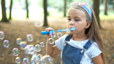 Yaz parkında sabun köpüğü üfleyen küçük mutlu kız çocuğu..
