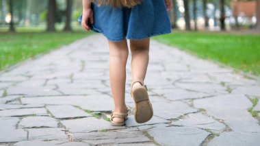 Yeşil parkta tek başına yürüyen yazlık elbiseli küçük bir kızın arka görüntüsü..