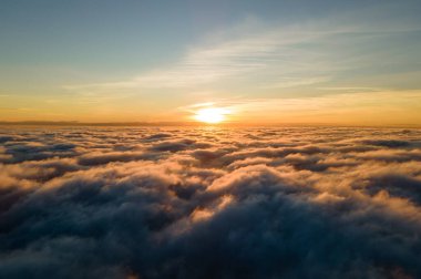 Üzerinde mavi gökyüzü olan beyaz yoğun bulutların üzerinde canlı sarı gündoğumunun havadan görüntüsü..
