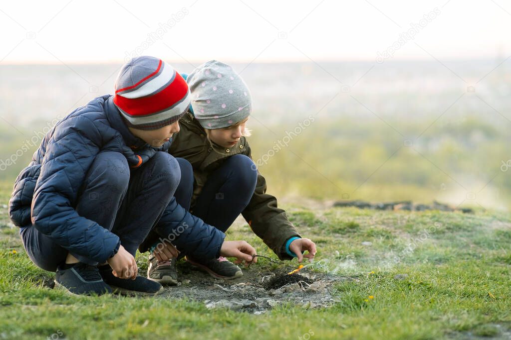Two children playing with fire outdoors in cold weather.