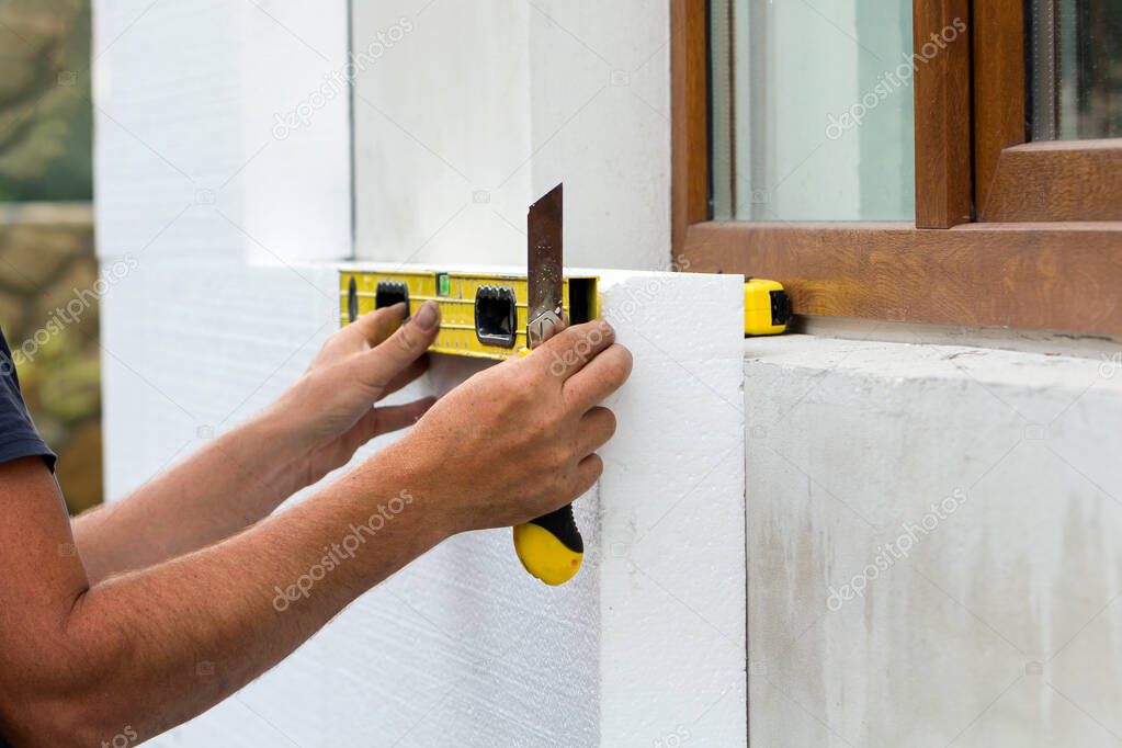 Construction worker insulating house wall with styrofoam insulatuion sheet.