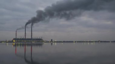 Kömür santrali yüksek borular siyah dumanlı geceleri hızlı hareket eden atmosferi gölün suyundaki yansımalarıyla kirletiyor. Günbegün zaman geçişi.