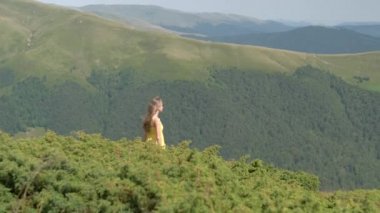 Sarı elbiseli genç bir kadın yaz dağlarında rüzgarlı bir günde çimlerin üzerinde yürüyor..