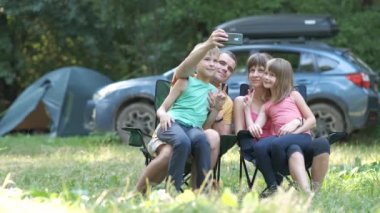 Genç ve mutlu bir aile kamp alanında birlikte dinleniyor ve cep telefonu kamerasıyla selfie çekiyorlar..