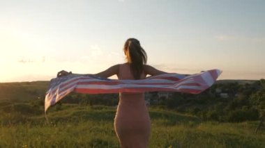 Gün batımında ABD bayrağıyla koşan mutlu genç bir kadının arka görüntüsü. Amerika 'nın bağımsızlık gününü kutlayan pozitif kız. Uluslararası Demokrasi Günü.