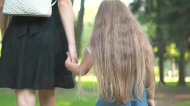 Annemin ve küçük kızının yaz parkında el ele yürürken görüntüsü..