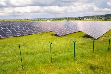 Yeşil alandaki güneş enerjisi santralinin koruyucu tel örgülü havadan görüntüsü. Temiz ekolojik enerji üretmek için elektrik panelleri.