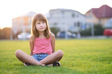 Genç mutlu kız sıcak yaz gününde yeşil çimlerde otururken dinleniyor.