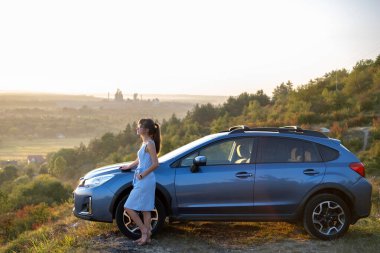 Genç bayan sürücü arabasının yanında dinleniyor sıcak yaz akşamının tadını çıkarıyor. Seyahat ve kaçış konsepti.