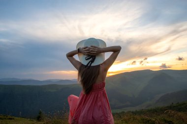 Kırmızılı genç kadın çimenli bir tarlada duruyor rüzgarlı bir sonbahar akşamında doğanın tadını çıkarıyor..