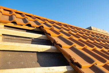 Üst üste binen sarı seramik çatı kiremitleri ahşap tahtalara monte edilmiş inşaat halindeki binanın çatısını kaplıyor..