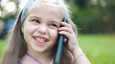 Mutlu küçük kız yaz parkında cep telefonuyla konuşuyor..