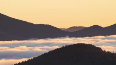 Gün doğumunda hareket eden sisli bulutlarla çevrili uzak karanlık dağ tepeleri..