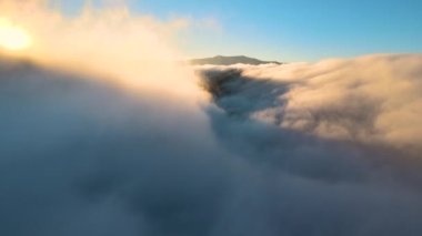 Sisli ve hızlı bulutların üzerindeki hava manzarası gün batımında dağ tepelerini kaplıyor..