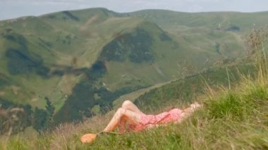 Kırmızı elbiseli genç bir kadın yeşil çimlere uzanıyor güneşli bir yaz gününde dinleniyor ve doğanın tadını çıkarıyor..