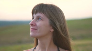 Kırmızı yaz elbisesi ve beyaz hasır şapkalı genç mutlu uzun saçlı kadın olgun altın buğdaylı sarı tarlada duruyor sıcak akşamın tadını çıkarıyor..