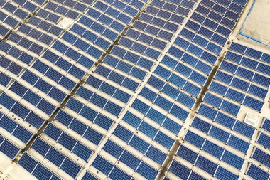 Sanayi binasının çatısına monte edilmiş mavi fotovoltaik panelleri olan güneş enerjisi santralinin hava görüntüsü.