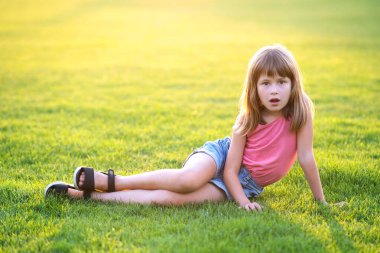 Genç ve güzel bir kız sıcak yaz gününde taze yeşil çimlerde oturuyor..