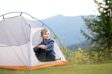 Mutlu çocuk dağ kampında turist çadırında tek başına dinleniyor ve güzel yaz manzarasının tadını çıkarıyor. Yürüyüş ve aktif yaşam biçimi.