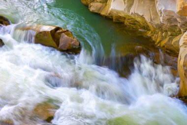 Nehir şelalesinin havadan görünüşü berrak turkuaz suyu kalın beyaz köpüklü ıslak kayaların arasına düşüyor..