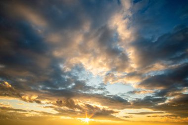 Turuncu batan güneş ve mavi gökyüzü tarafından aydınlatılan kabarık bulutlarla dramatik günbatımı manzarası.