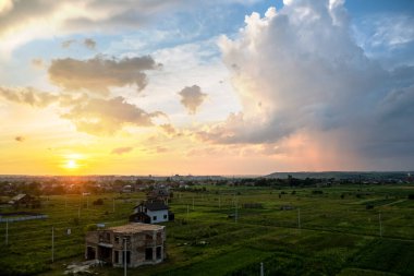 Turuncu batan güneş ve mavi gökyüzü ile aydınlanan kabarık bulutlu kırsal bölgenin dramatik günbatımı manzarası.